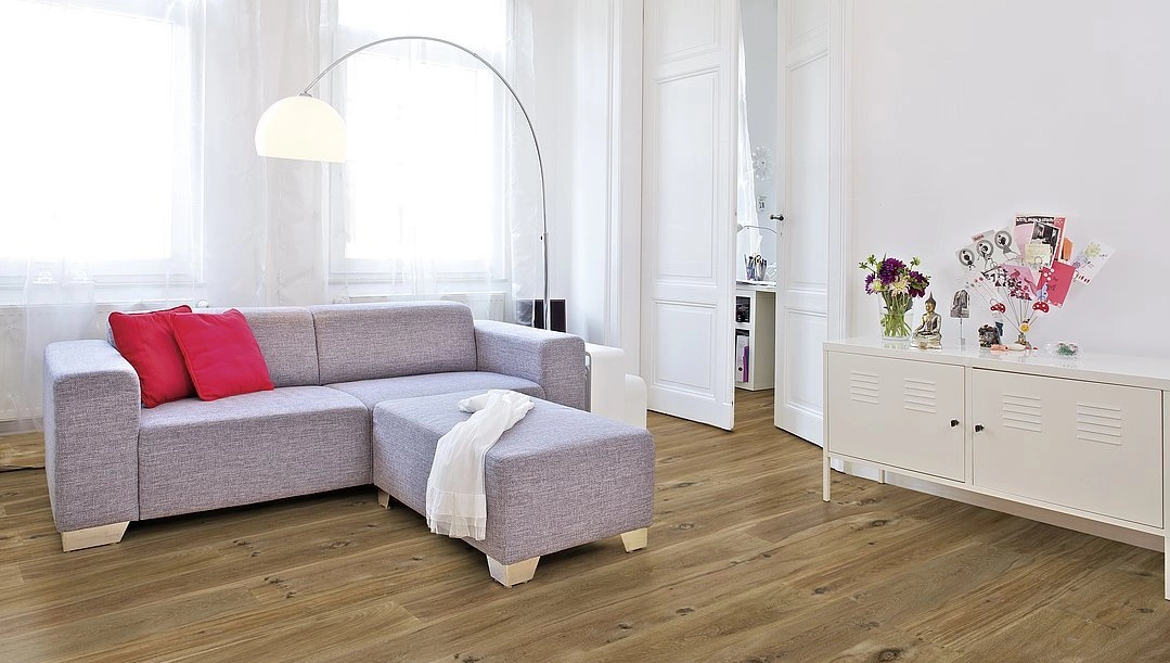 Dunkler Parkettboden verlegt in einem Wohnzimmer mit pinkgrauer Couch. Rechts auf dem Bild ist ein kleines Sideboard zu sehen worauf Blumen stehen. Dunkler Parkettboden verlegt in einem Wohnzimmer mit pinkgrauer Couch. Rechts auf dem Bild ist ein kleines Sideboard zu sehen worauf Blumen stehen.